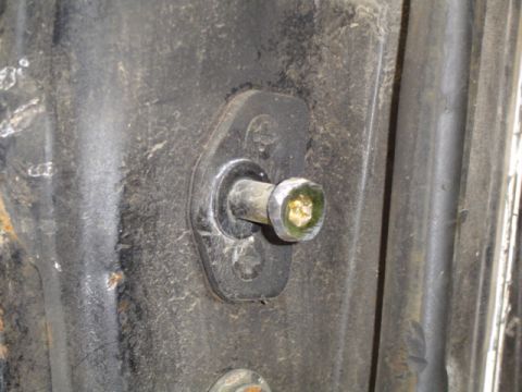 1979 Ford Bronco - Extreme close-up of a door striker post bolted to a weathered black body pillar, the polished pin head showing yellow-green plating through…