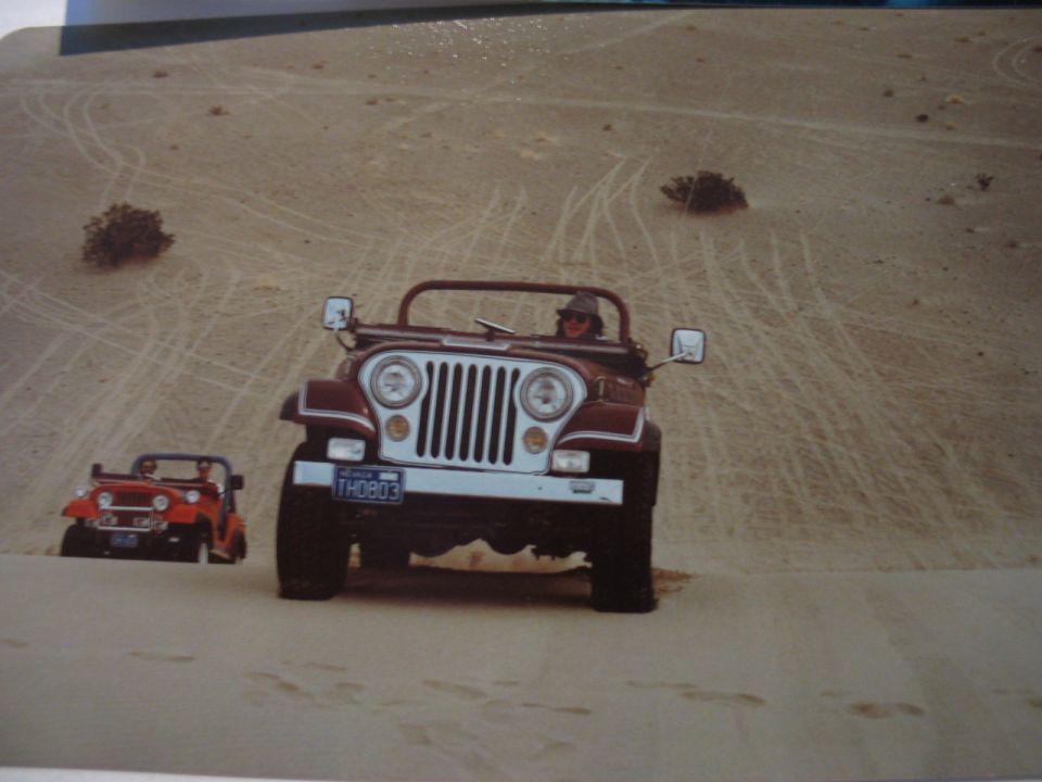 Two Jeeps driving on sand dunes, one red and one maroon