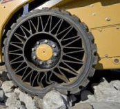 1990 Ford Bronco - yellow construction machine fitted with a black airless tire featuring honeycomb spoke webbing, parked on rocks.