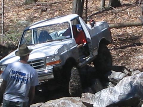 1995 Ford Bronco - A white Ford F-150 truck navigates a rocky trail with its driver's door ajar.