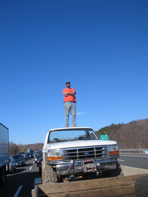 1995 Ford Bronco - A man stands atop a modified pickup truck on a highway, with other vehicles visible in the background.