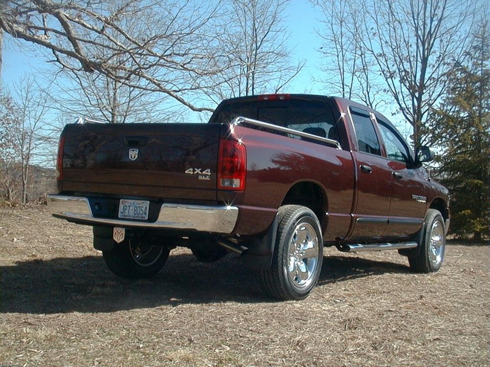 Dark maroon Dodge Ram 4x4 quad cab pickup, rear three-quarter view, chrome bed rails and wheels, outdoors