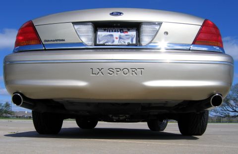 2000 Ford Crown Victoria - Ground-level straight-on rear shot of a gold Ford Crown Victoria, showing "LX SPORT" lettering across the bumper, the Crown Victoria badge…