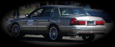 2001 Mercury Grand Marquis - A gray 2001 Mercury Grand Marquis is seen from the rear three-quarter angle, with racing numbers on its side.