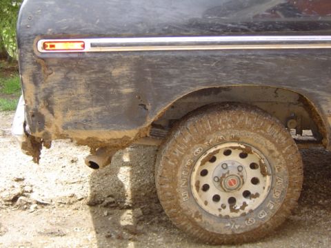 1979 Ford Bronco - The rear fender and tire of a dirty vehicle are visible, with mud splattered on the body and wheel.