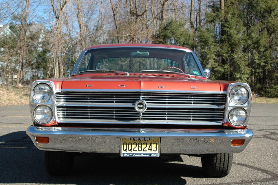 Front view of red 1960s Ford Fairlane with chrome grille and dual headlights