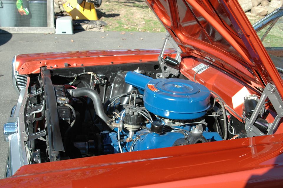 Engine bay of orange classic Ford with blue engine and round air cleaner, hood up