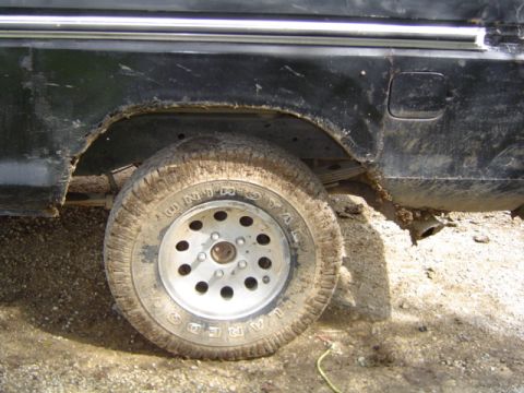 1979 Ford Bronco - The rear wheel well of a black truck shows significant rust and mud accumulation around the tire.