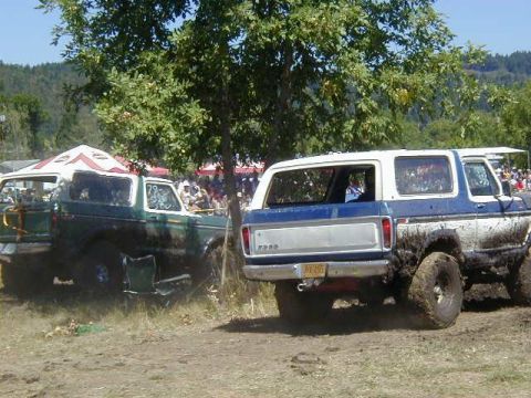 1978 Ford Bronco - Two muddy Ford Broncos are parked in a field, one behind the other.