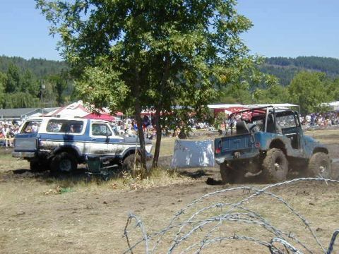 1978 Ford Bronco - Two off-road vehicles are stuck in the mud during an event, with a crowd watching in the distance.