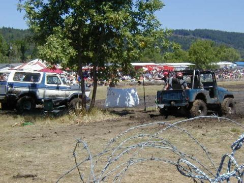 1978 Ford Bronco - A blue and white Ford Bronco is seen in a muddy field with a crowd in the background.
