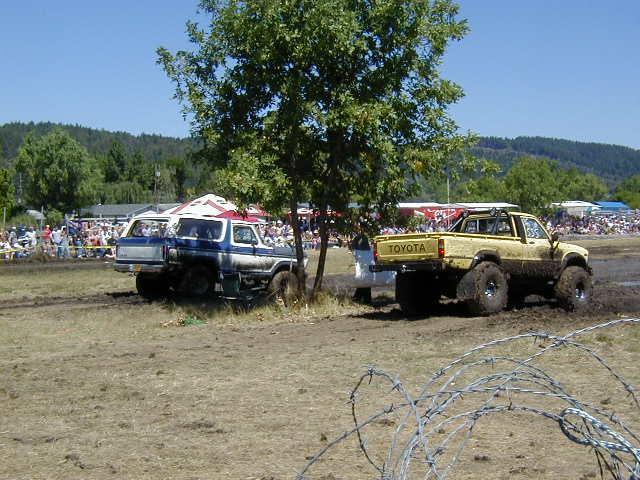 Blue and white SUV parked next to a yellow Toyota pickup truck in a muddy field