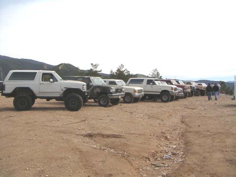 1988 Ford Bronco - Several SUVs and trucks are parked in a line on a dusty, outdoor lot with hills in the background.