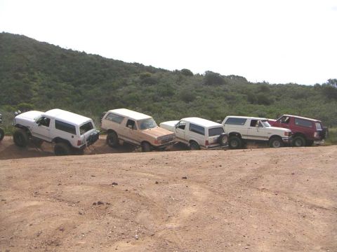 1988 Ford Bronco - A group of Ford Broncos are lined up on a dusty trail, ready for an off-road adventure.