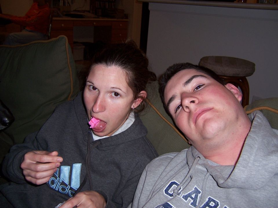 Woman with pink candy on her tongue and man looking at camera, both on a couch