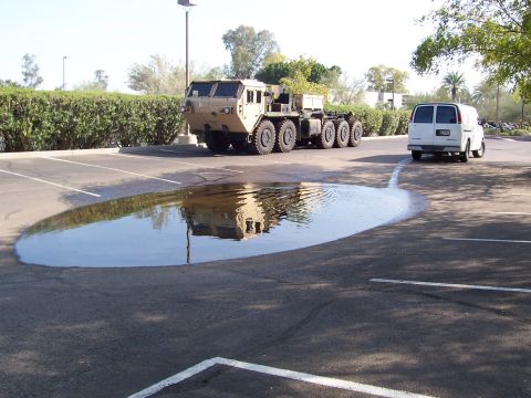 1994 Ford Bronco - A large military truck and a white van are parked in a lot, with a significant puddle reflecting the truck.