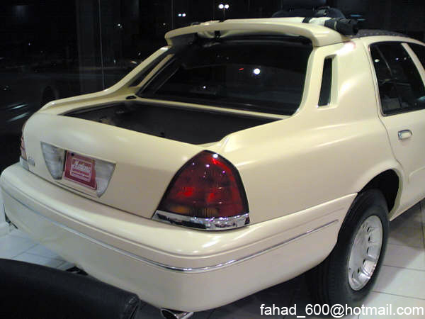 Rear of a cream-colored sedan with a spoiler and open trunk. License plate frame visible