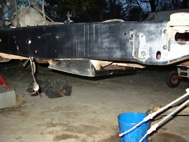 Freshly painted black truck frame rail on stands outdoors at dusk, tools and blue bucket nearby