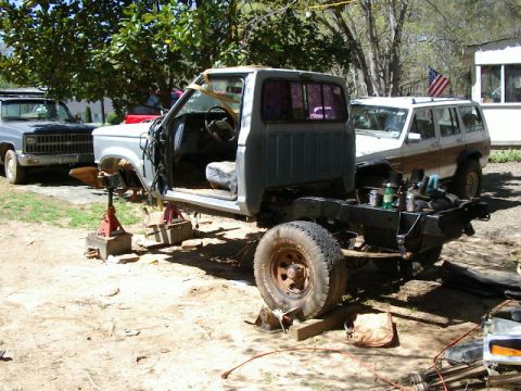 1985 Ford Bronco - 1985 Ford Bronco undergoing repairs, chassis elevated on jack stands in a yard.