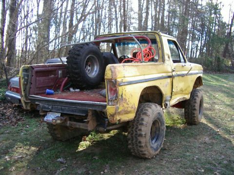 1985 Ford Bronco - Modified yellow pickup truck with large tires and a spare tire mounted in the bed, parked outdoors.