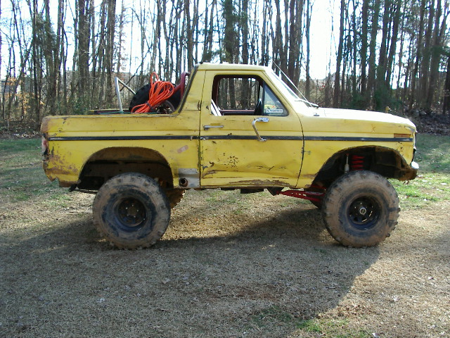 yellow pickup truck with off-road tires and suspension, spare tire and orange rope in bed