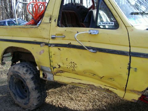 1985 Ford Bronco - This yellow 1985 Ford Bronco shows significant wear and tear, including a heavily dented door and off-road tires.