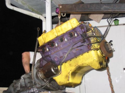1985 Ford LTD Crown Victoria - Engine and transmission assembly being lifted by a hoist, with a person's arm visible in the background.