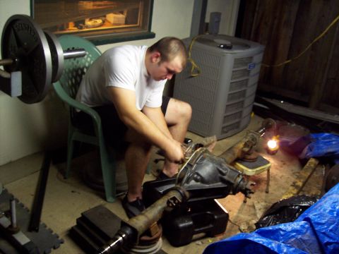1988 Ford Bronco - A person works on a vehicle differential, with gym weights and an air conditioning unit visible in the cluttered garage setting.
