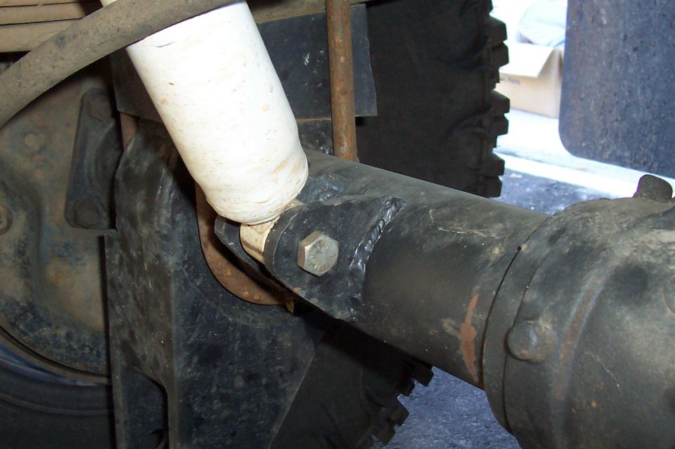 Close-up of a vehicle's rear axle and shock absorber assembly. Shows a white shock with black mounting hardware and a bolted axle