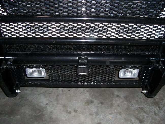 Front of a truck with a black grille and bumper, fog lights visible