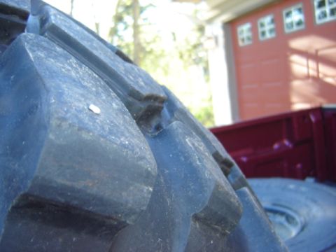 1992 Ford Bronco - Detail of a large tire tread, with a portion of a red truck bed in the background.