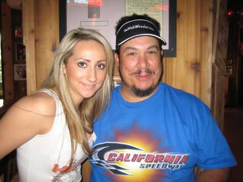1990 Ford Bronco - blond woman and a man wearing a blue California Speedway shirt and black visor pose together inside a wood-paneled bar.