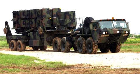 1988 Ford Bronco - A heavy-duty military truck transports a missile launcher system, seen from a three-quarter front view on a dirt path.