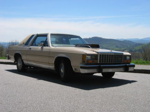 1985 Ford LTD Crown Victoria - Front three-quarter view of a tan/beige two-door Ford Crown Victoria coupe with a padded vinyl half-roof, chrome grille and bumpers, hood s…