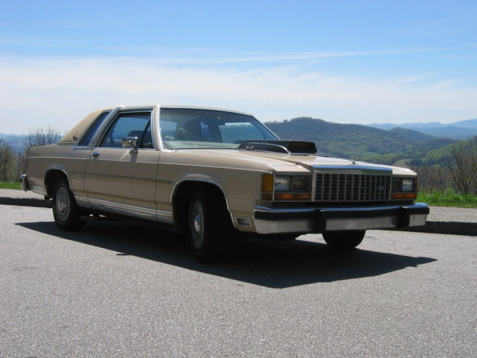 Tan two-door Ford Crown Victoria coupe with hood scoop, front three-quarter view at mountain overlook