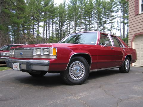 1991 Ford LTD Crown Victoria - A red sedan is parked in a driveway with trees in the background.