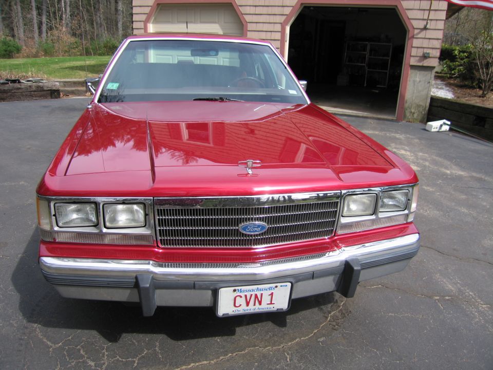 Front view of a red Ford sedan parked in a driveway. The grille has a Ford logo. License plate reads CVN 1