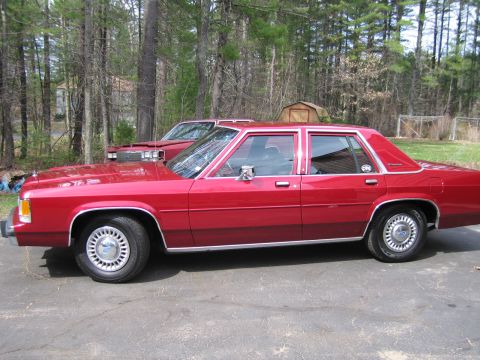 1991 Ford LTD Crown Victoria - A red Ford Crown Victoria sedan is parked in a driveway with trees in the background.