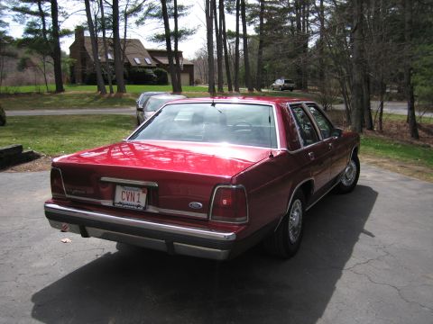 1991 Ford LTD Crown Victoria - A red sedan is parked in a driveway with a house and trees in the background.