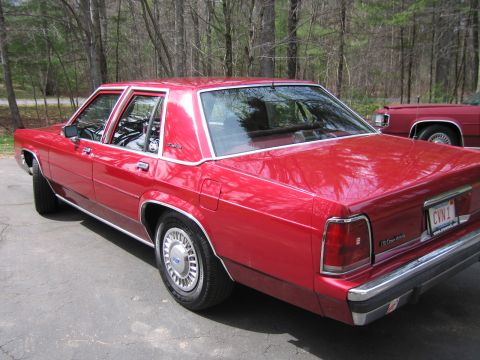 1991 Ford LTD Crown Victoria - A red 1991 Ford Crown Victoria LTD sedan is parked outdoors, with another red vehicle visible in the background.