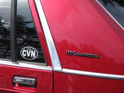 1991 Ford LTD Crown Victoria - Close-up of a red car's side panel, showing chrome trim and a 'LTD Crown Victoria' emblem.