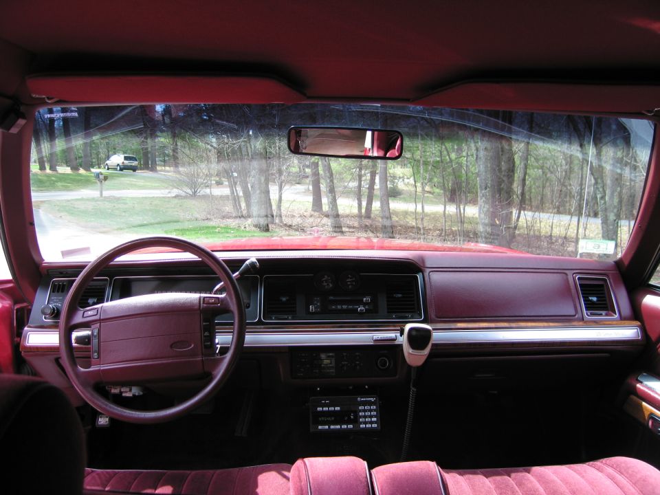Interior view of a maroon car, showing the dashboard, steering wheel, and seats. A white SUV is visible outside through the windshield