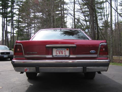 1991 Ford LTD Crown Victoria - The rear of a red 1991 Ford Crown Victoria LTD is shown, with a license plate and a second vehicle visible in the background.