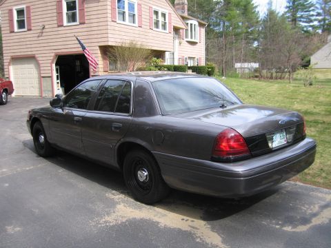 1991 Ford LTD Crown Victoria - The rear of a dark gray Ford Crown Victoria is visible, parked in front of a house and garage.