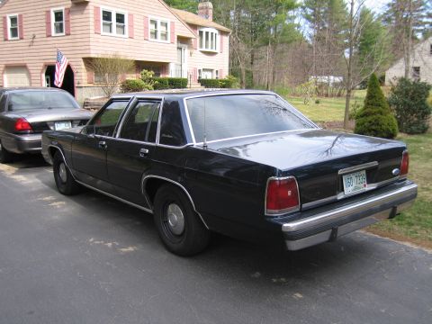 1991 Ford LTD Crown Victoria - A dark sedan is parked on a driveway next to another vehicle, with a house in the background.
