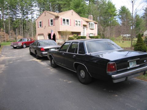 1991 Ford LTD Crown Victoria - A black 1991 Ford Crown Victoria LTD is parked in a driveway behind another sedan, with a red car in the background.