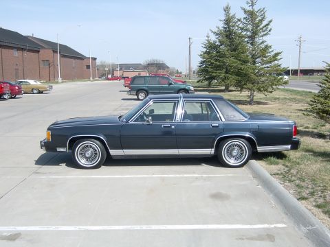 1990 Ford Crown Victoria - A 1990 Ford Crown Victoria sedan is parked in a lot, showing its side profile.