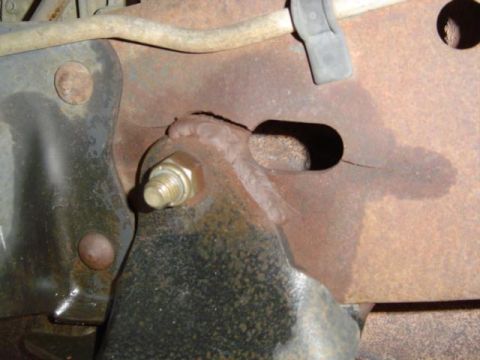 1988 Ford Bronco - Detail of a rusted metal frame component, showing a bolt and bracket assembly.