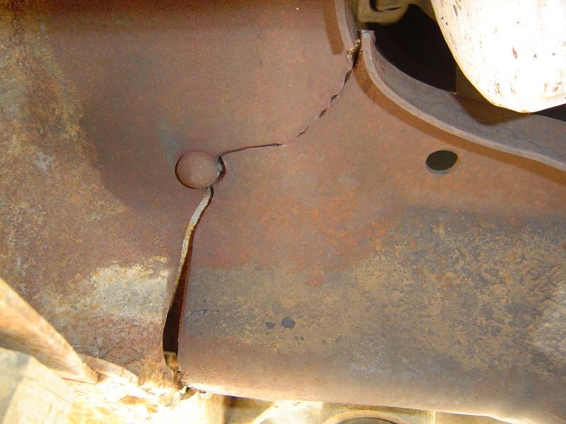Close-up of heavily rusted metal frame showing a large crack and a bolt head