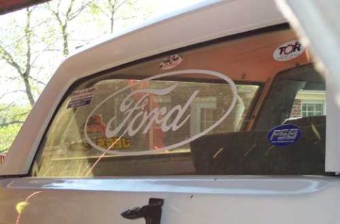 1988 Ford Bronco - The rear window of a 1988 Ford Bronco displays the iconic Ford logo and several other stickers.